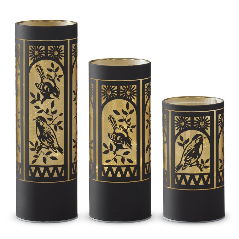 Set of 3 matte black glass LED cylinder lanterns with gold bird silhouettes and floral accents on a white background.