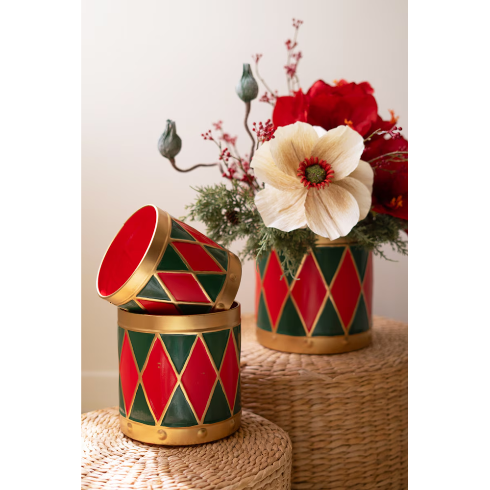 Three metal Christmas drum planters styled on woven stools, one stacked and one with florals.