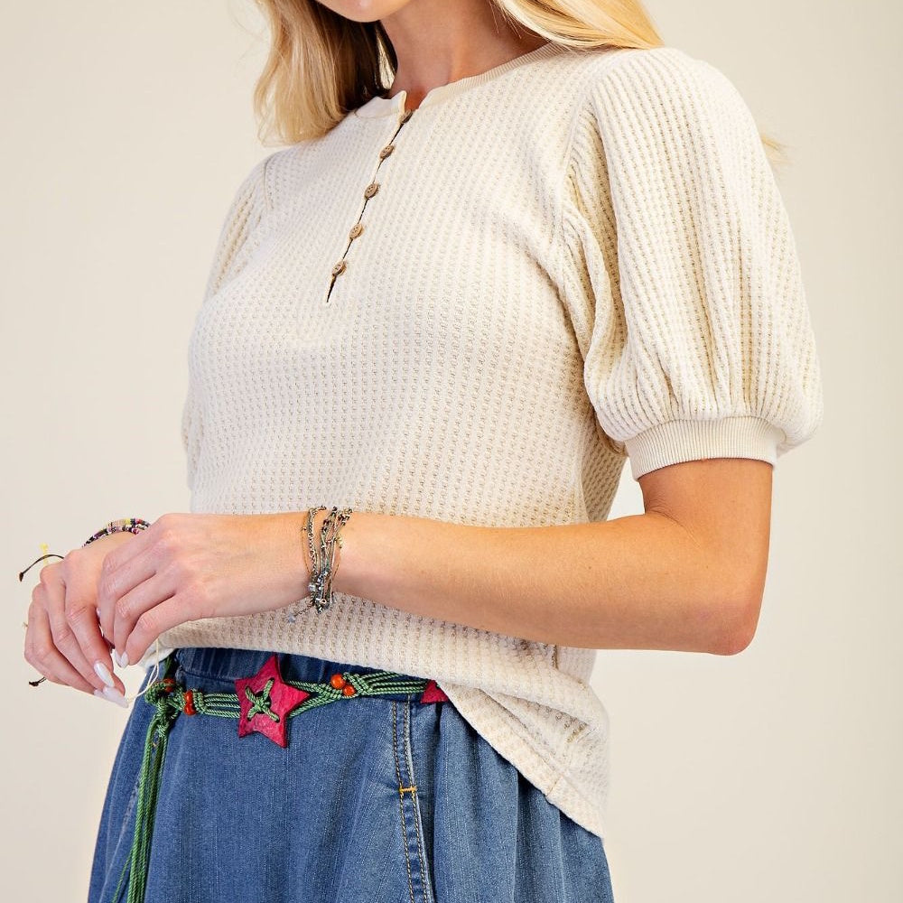 Woman wearing a cream mineral wash waffle knit top with puff sleeves and button detail.