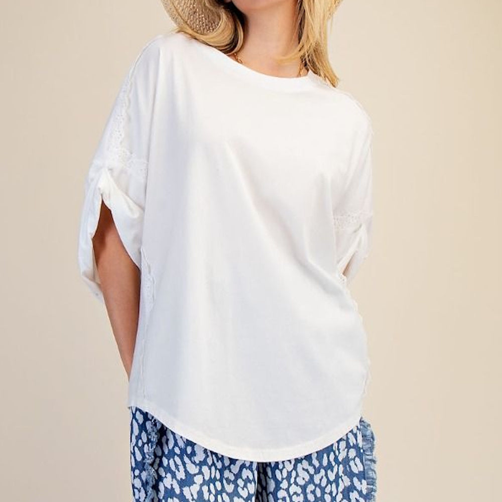 Woman wearing a white short-sleeve top with lace detail and blue patterned shorts against a neutral background.