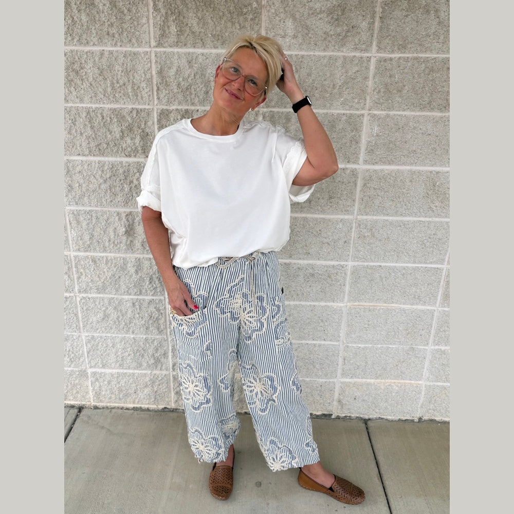 Woman in white t-shirt and blue striped floral pants standing against a brick wall.
