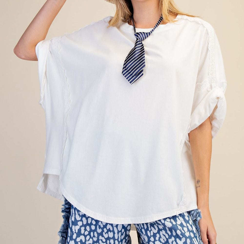 Woman wearing an oversized white top with lace trim, a blue striped necktie, and patterned pants.