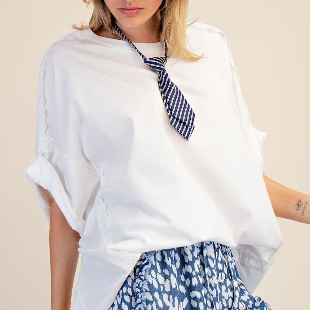 Woman in oversized white lace-trim top with striped tie and blue leopard print shorts against a cream background.