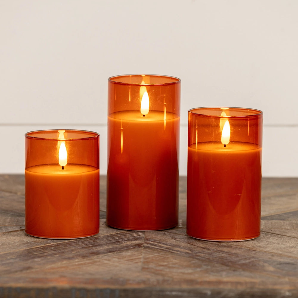 Three amber glass flameless pillar candles of varying heights glowing on a wooden table.
