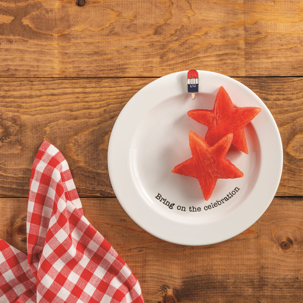 Star-shaped watermelon on a "Bring on the celebration" plate with a patriotic popsicle charm on a wooden table.