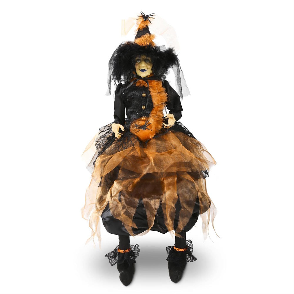 Sitting witch figurine with a pointed hat and a layered black and orange tulle dress.