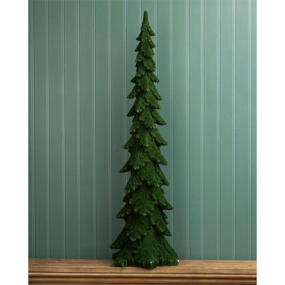 Single tall, slim green velvet decorative pine tree on a wooden surface against a wall.