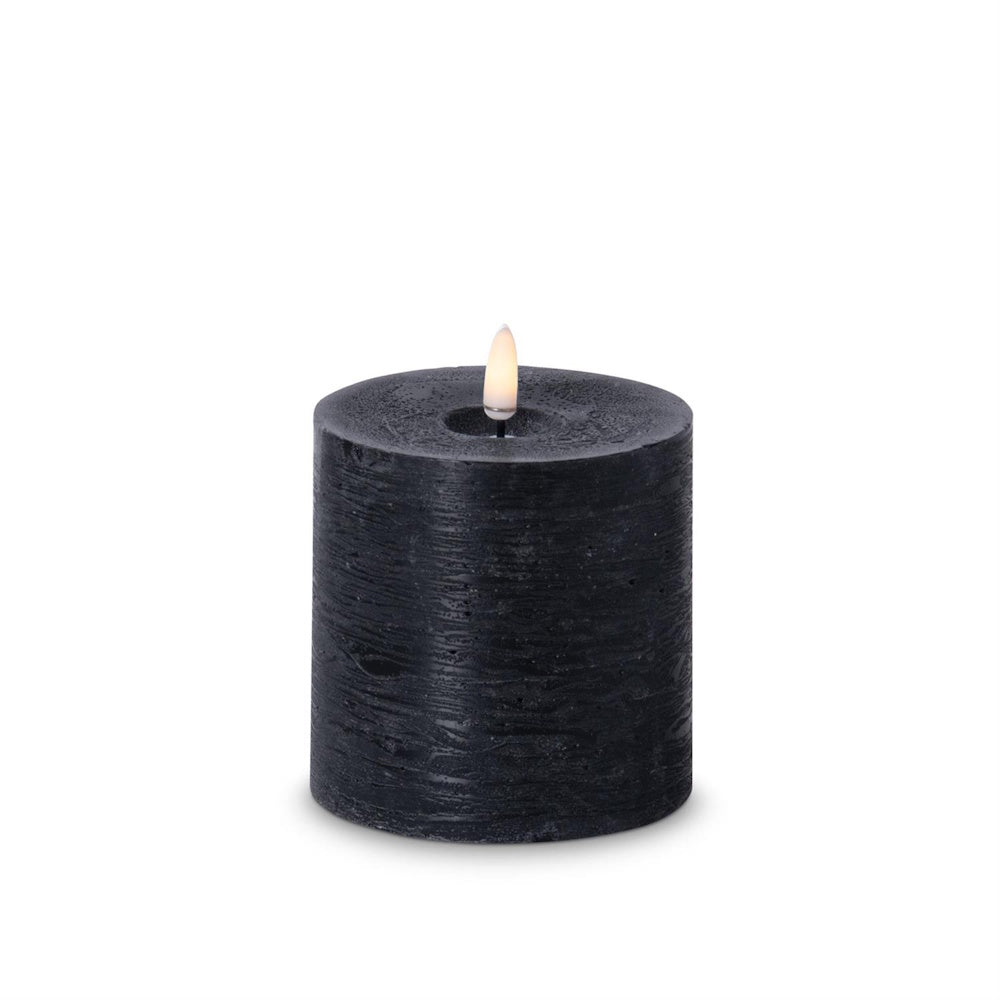 Small black textured flameless LED pillar candle with a warm glowing faux flame.
