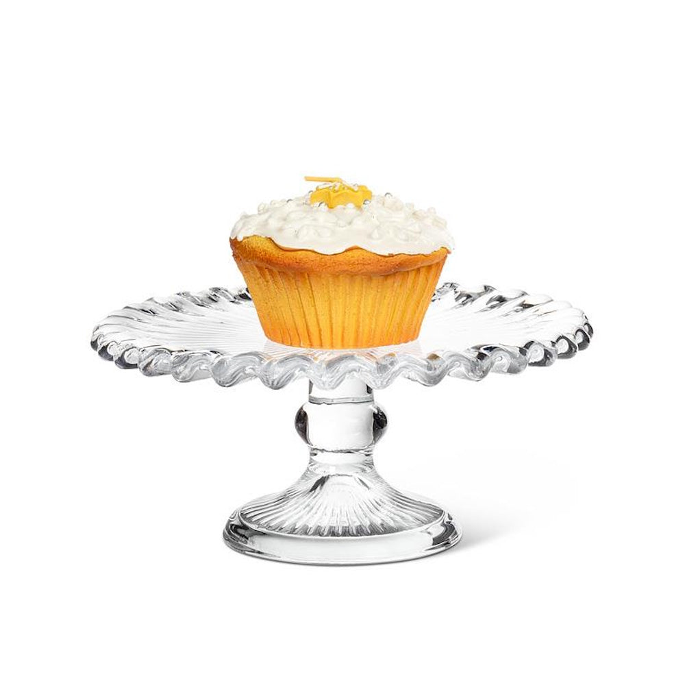 Cupcake with white frosting on a clear glass mini pedestal cake stand with a ruffled edge.