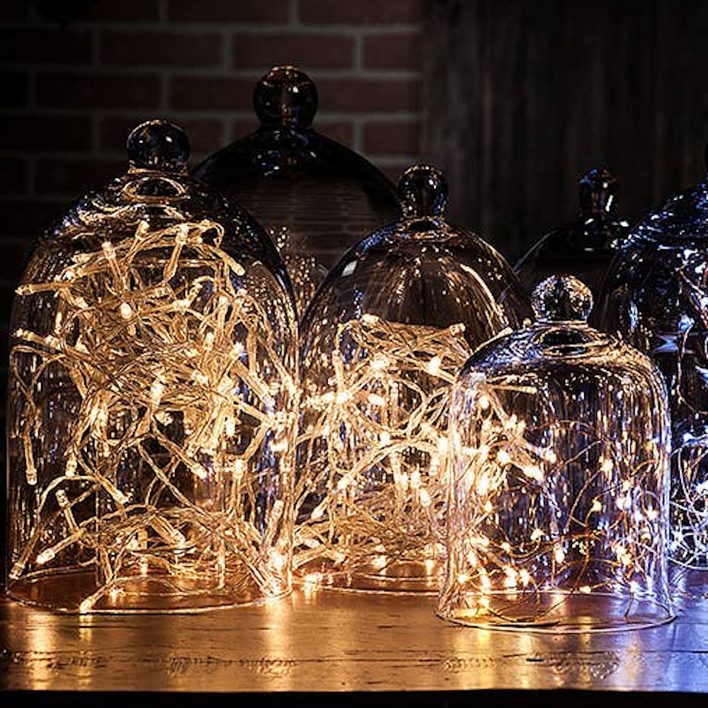 Glass cloches filled with warm glowing fairy lights displayed on a wooden table.