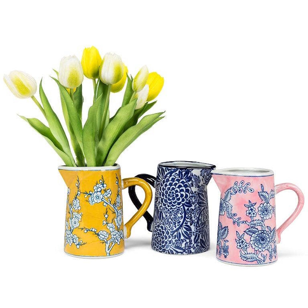 Three small floral ceramic pitchers in yellow, blue, and pink, with yellow tulips in the yellow jug.