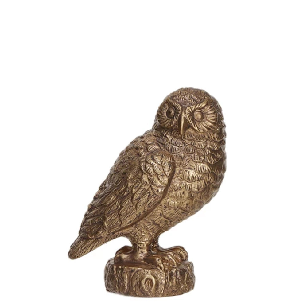 A small, detailed bronze or gold-finish owl figurine perched on a tree stump against a white background.