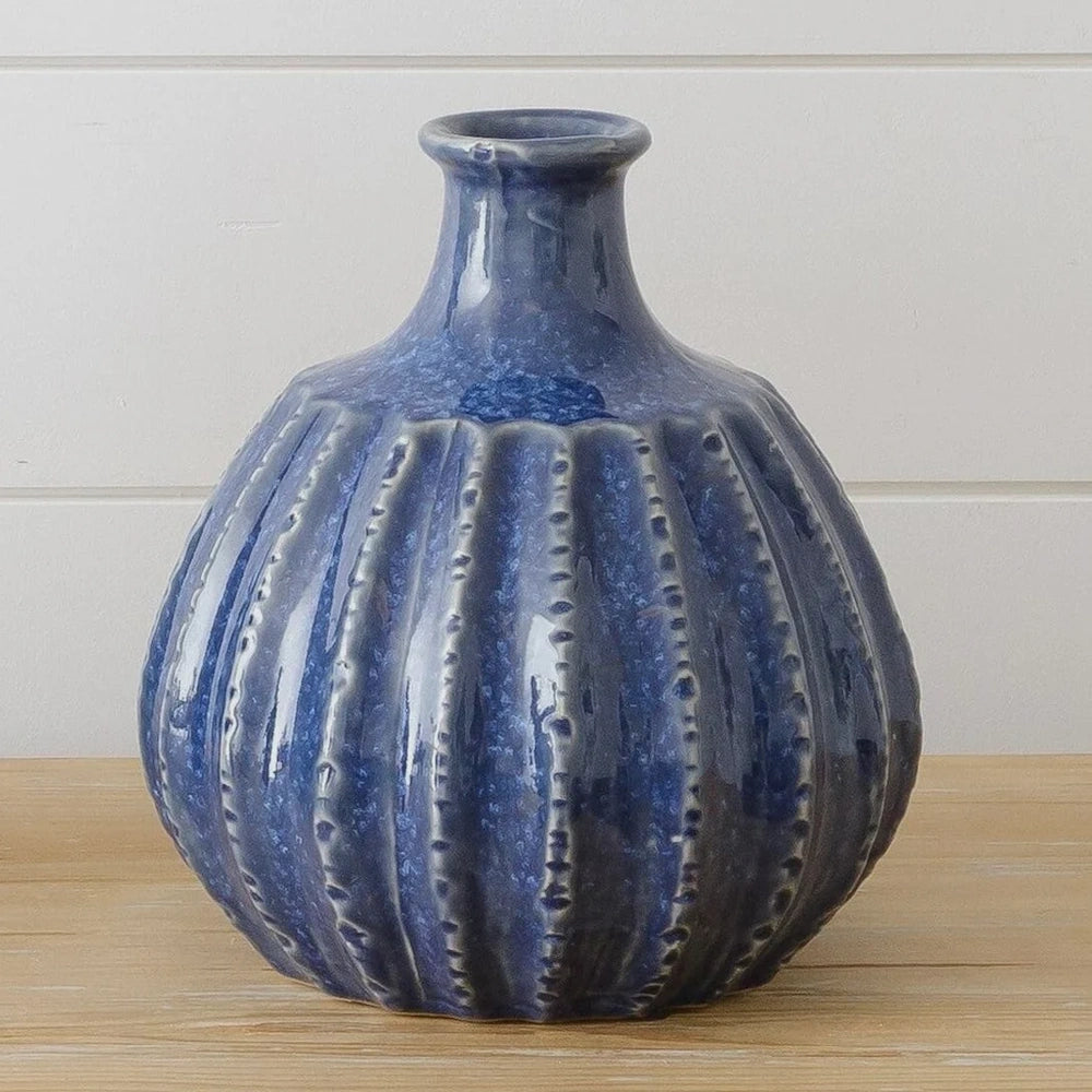 A ribbed, round blue ceramic vase with a narrow neck sitting on a wooden surface.