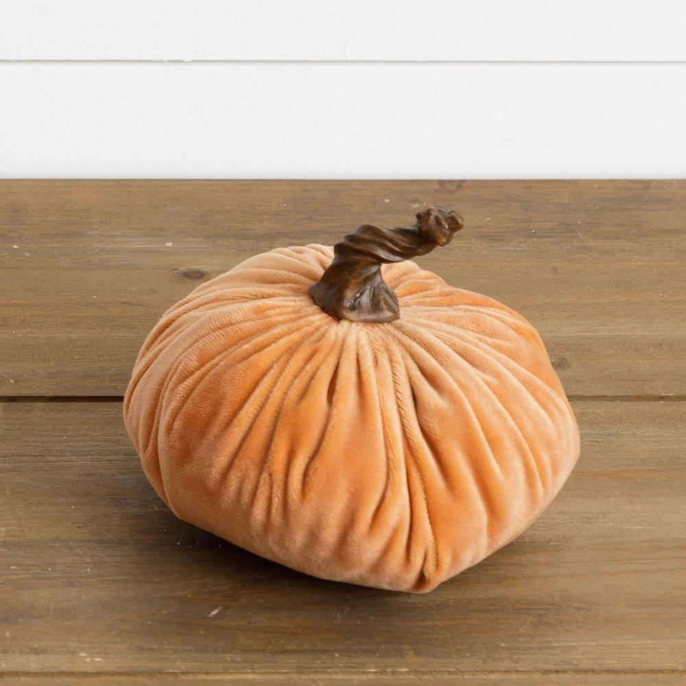 Plush soft orange velvet decorative pumpkin with a brown twisted stem on a wooden surface.