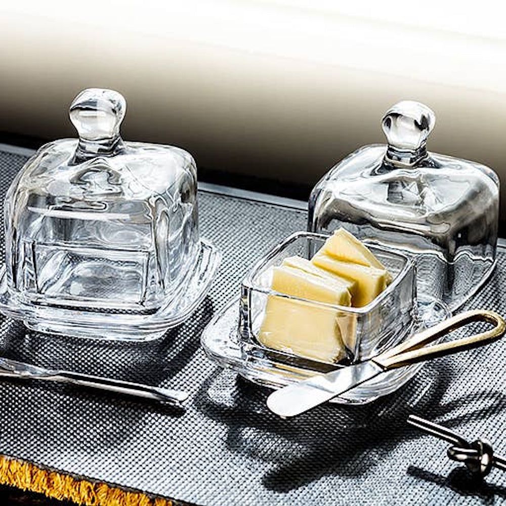 Clear glass covered butter dishes, one open containing butter, paired with a small butter knife.