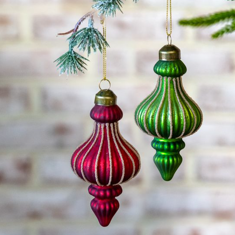 Red and green ribbed glass finial ornaments with glitter details hanging on pine branches.