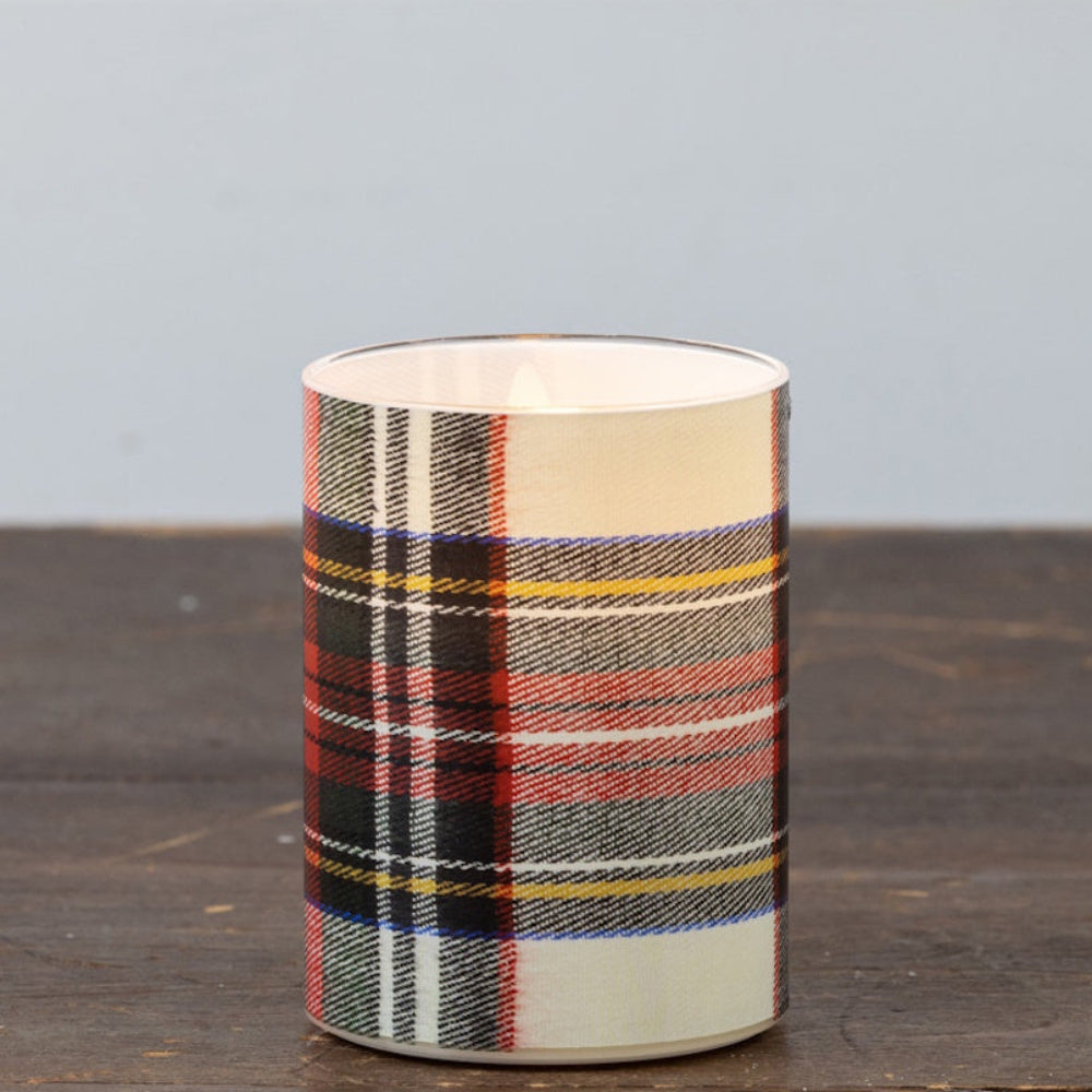 A single glowing white tartan plaid pillar candle on a rustic wooden table.