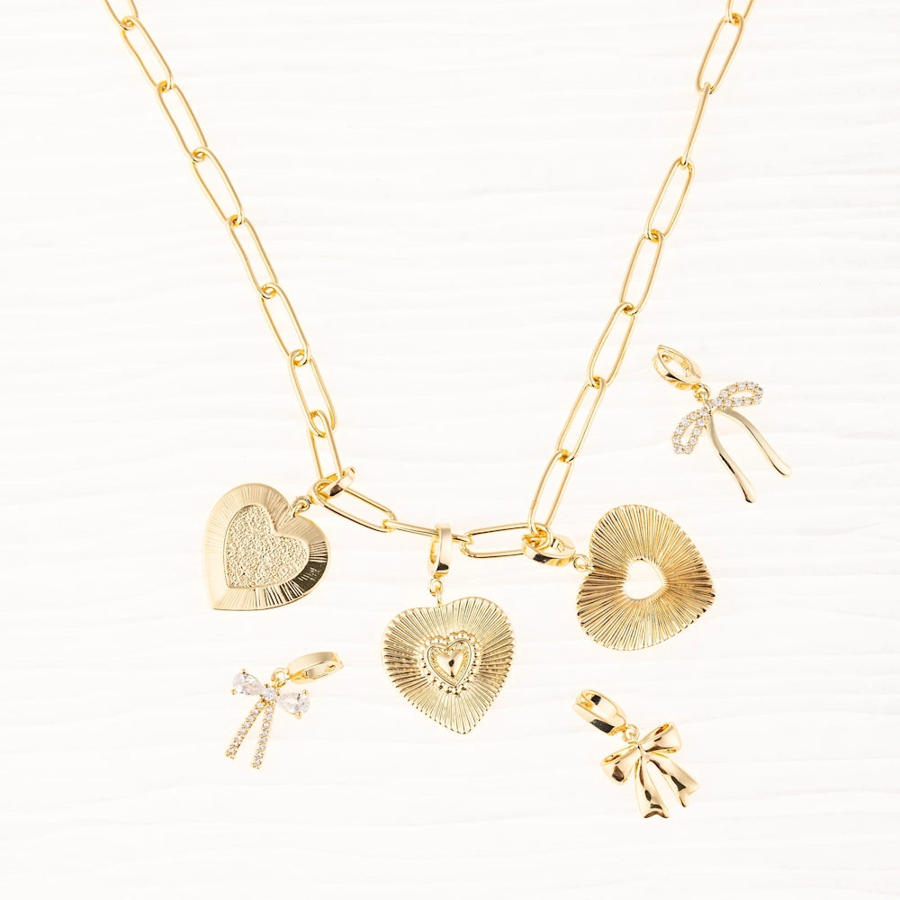 Gold link chain necklace with textured heart charms, surrounded by bow-shaped charms on white background.