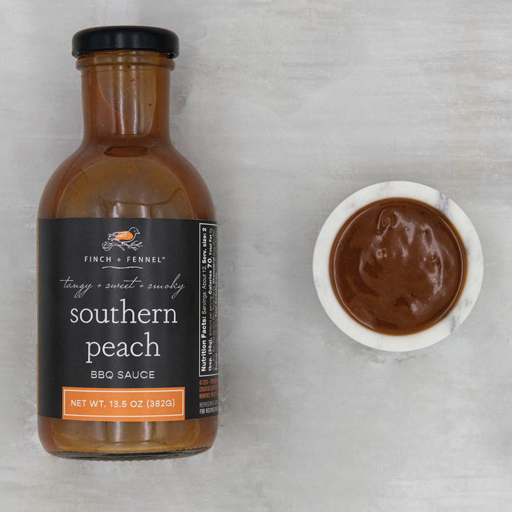 A bottle of Finch + Fennel Southern Peach BBQ sauce next to a small marble bowl filled with sauce.
