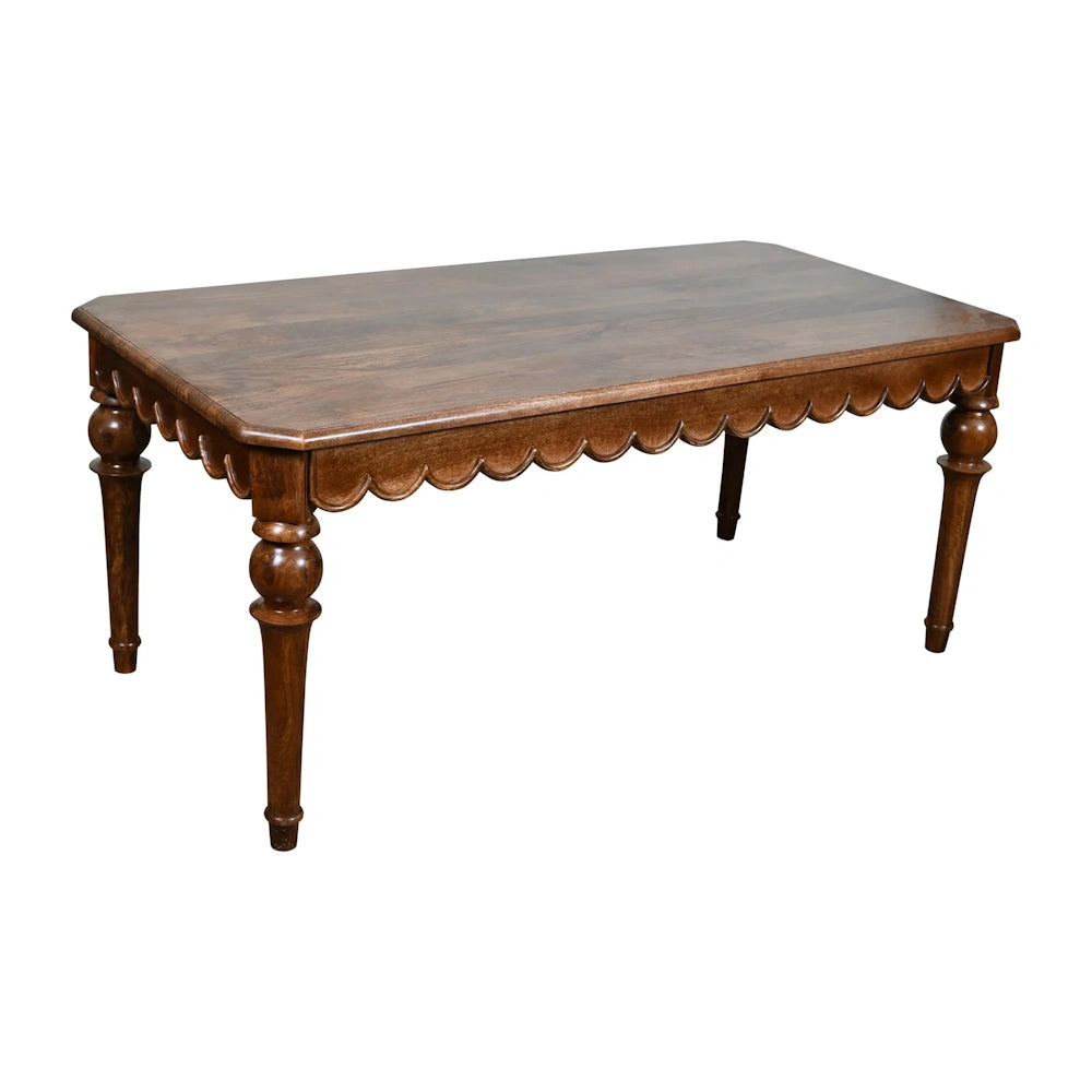 Rustic dark wood dining table with scalloped apron and turned legs on white background.