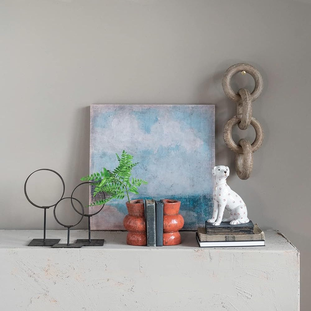 Square beach canvas art on a mantel with books, a dog figurine, and decorative objects.