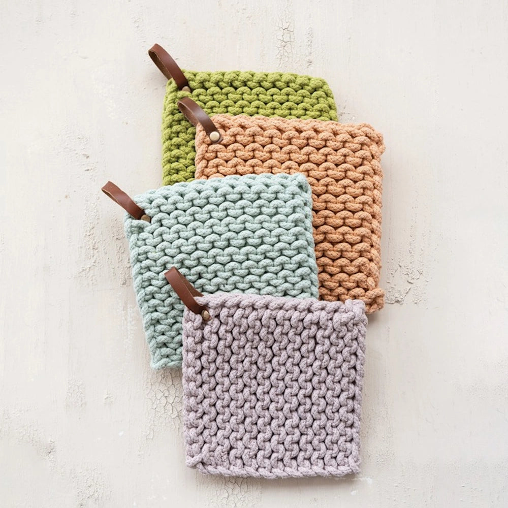 Stacked square cotton crochet pot holders in green, tan, blue, and purple with brown leather hanging loops.