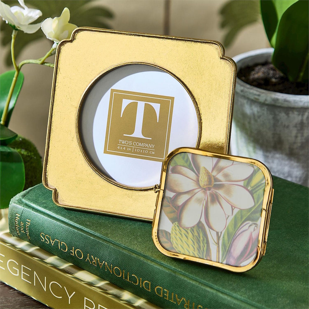Two gold picture frames rest on a stack of books, one displaying a flower print.