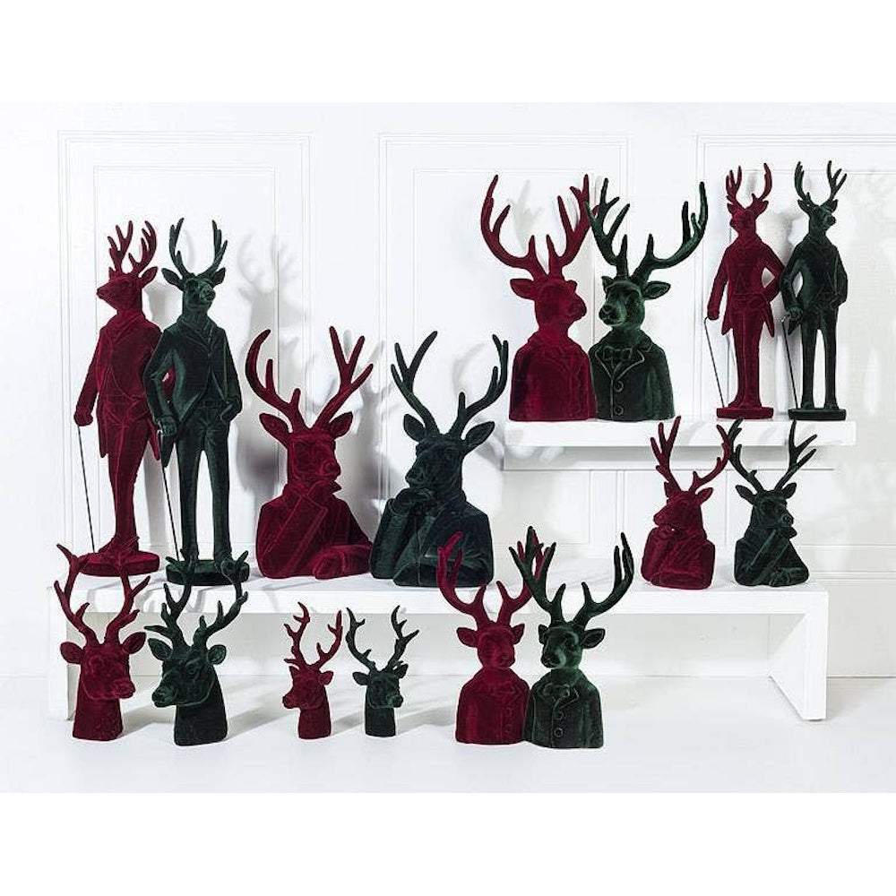 Red and green velvet stag and deer busts and full-body figurines wearing suits on white shelves.