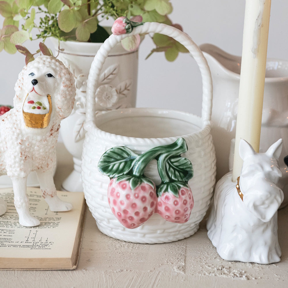 White strawberry ceramic basket displayed with vintage dog figurines and hydrangeas in a cottagecore home setting.