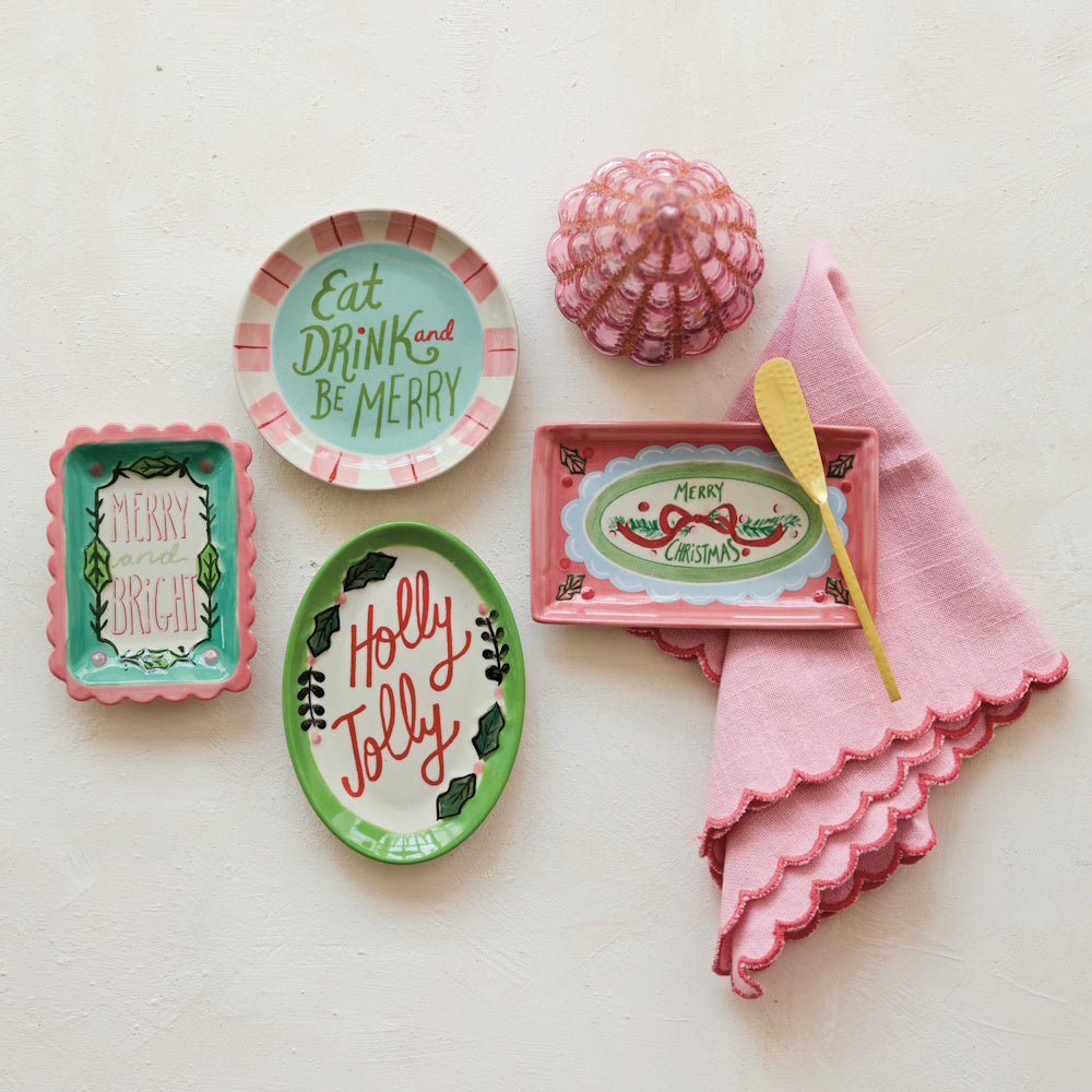 Flat lay arrangement featuring holiday stoneware dishes, a pink napkin, a spreader knife, and a pink decorative tree on a neutral surface.