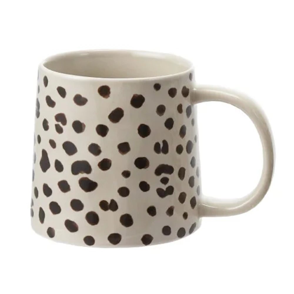Cream ceramic coffee mug with black leopard print spots and large handle on white background.