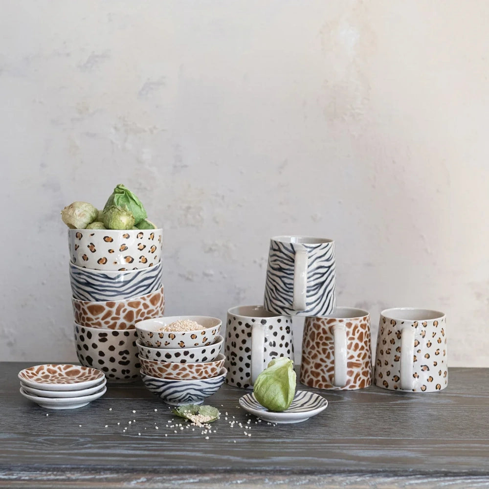 Animal print ceramic dinnerware set including mugs, bowls, and plates with leopard, zebra, and giraffe patterns.
