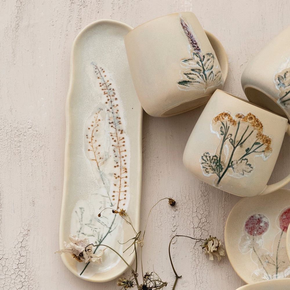 Lifestyle view of an organic-shaped stoneware platter and matching floral-designed mugs arranged together.