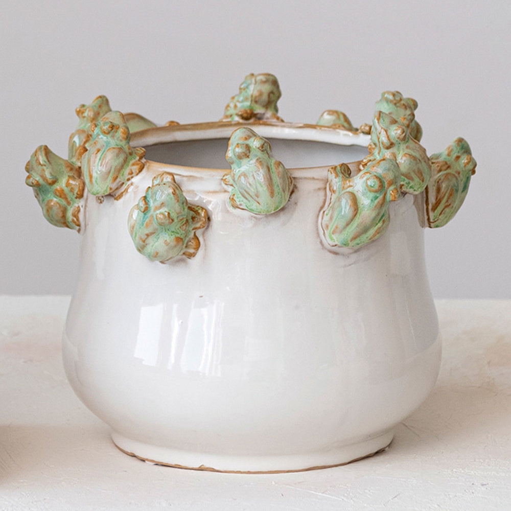 White stoneware planter with small green ceramic frogs climbing around the upper rim.