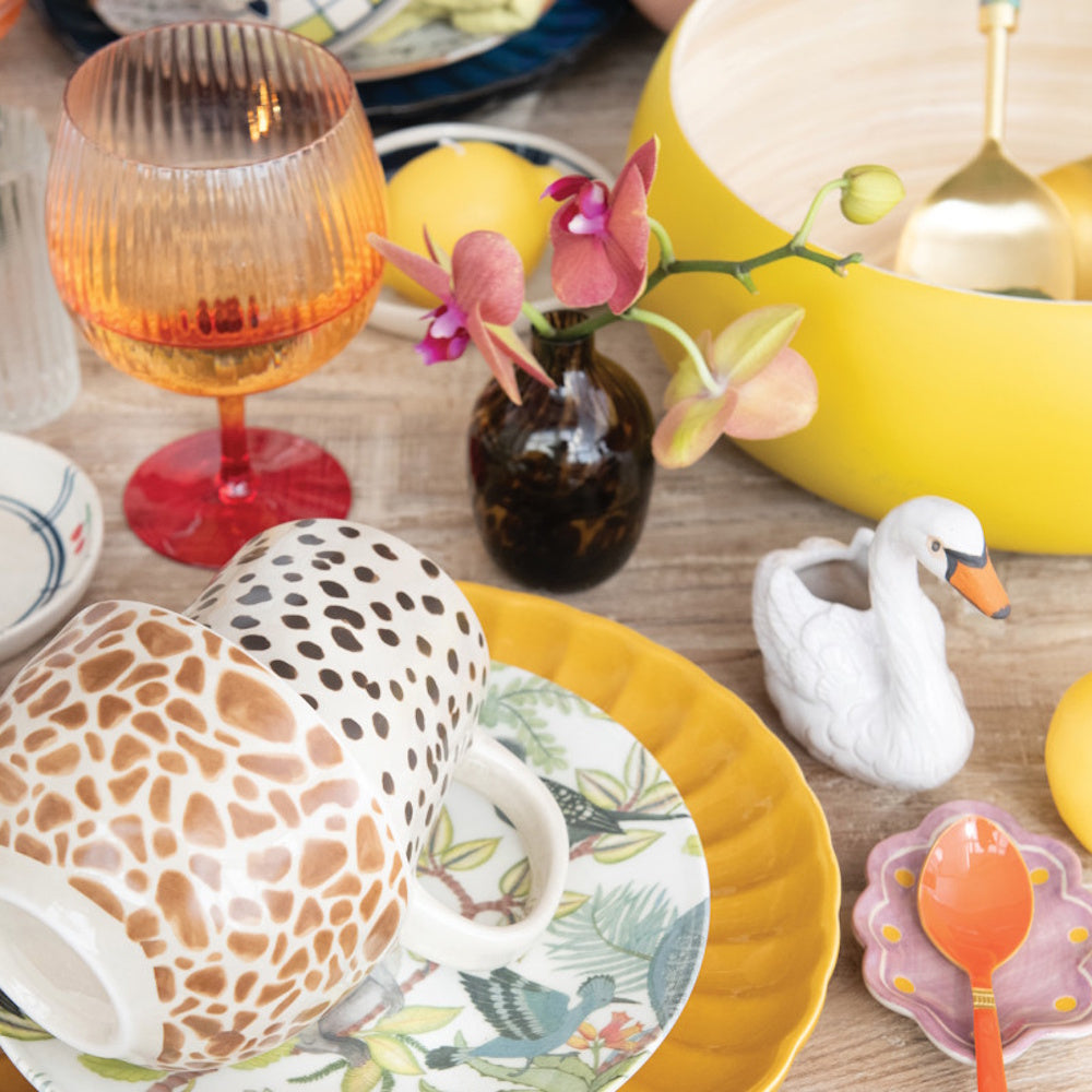 White stoneware swan-shaped toothpick holder placed on a dining table alongside patterned mugs, a yellow bowl, and tableware.