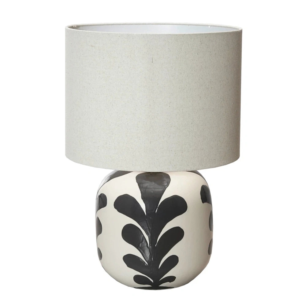 Stoneware table lamp with a black abstract leaf design and a neutral linen drum shade on a white background.