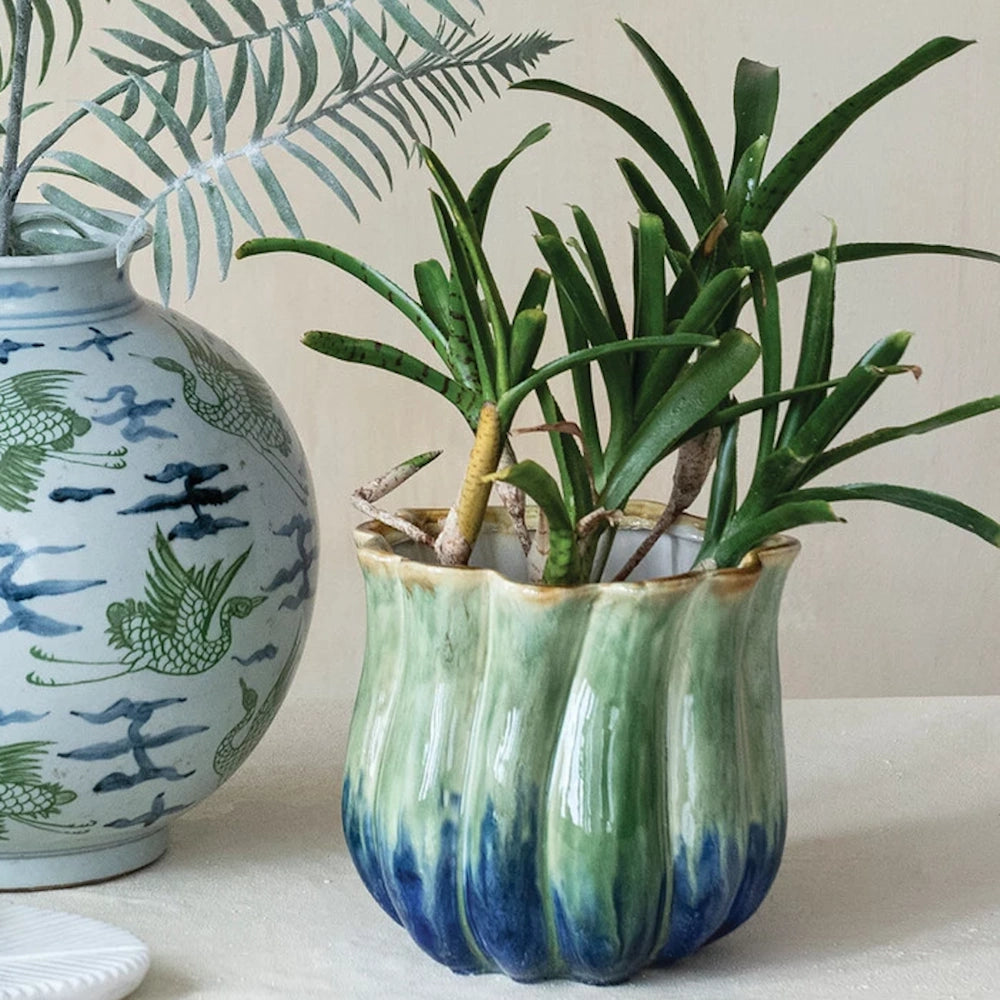 Two-tone green and blue fluted stoneware planter with a small green plant next to a crane-patterned ceramic vase.