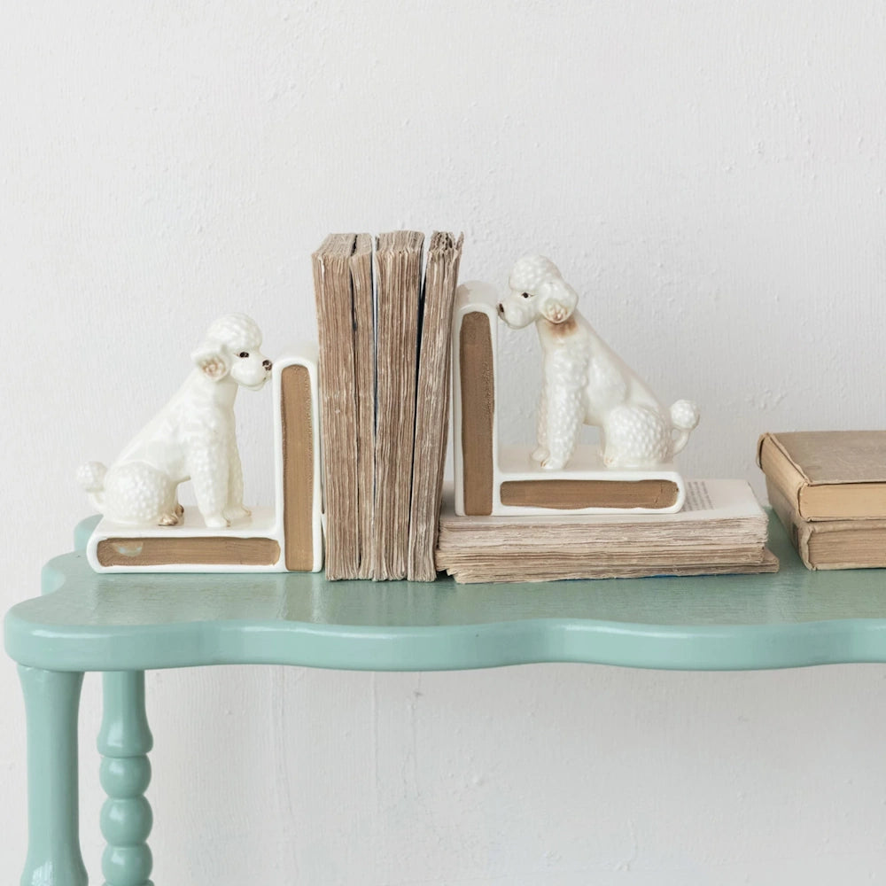 Vintage white ceramic poodle bookends holding books on a teal console table.