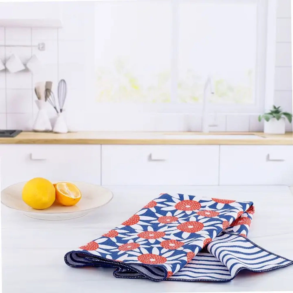This patterned dish towel has orange and blue flowers and stripes on a white counter next to lemons in a bright kitchen.