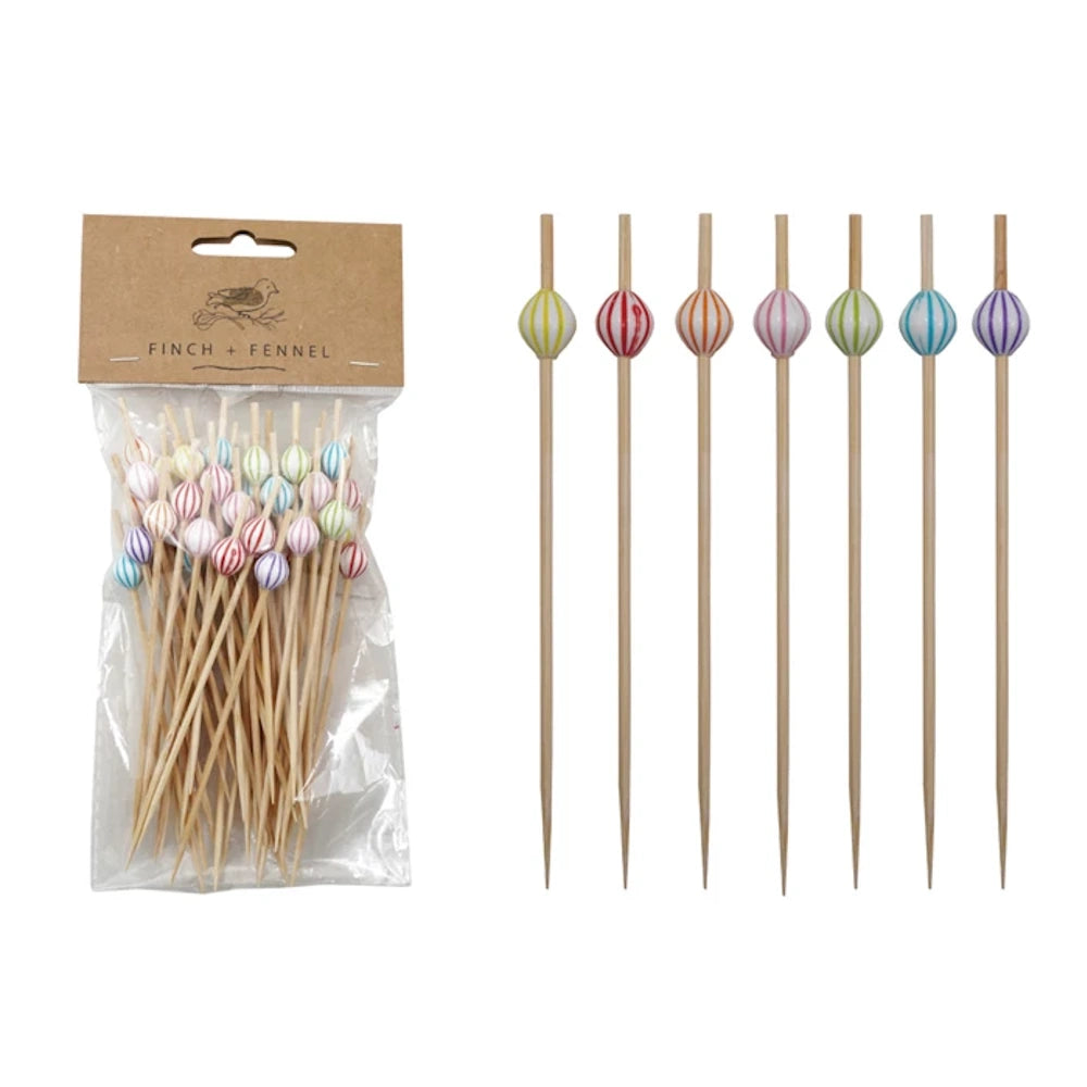 Packaged bamboo food picks next to a row of seven individual picks with colorful striped decorative beads.