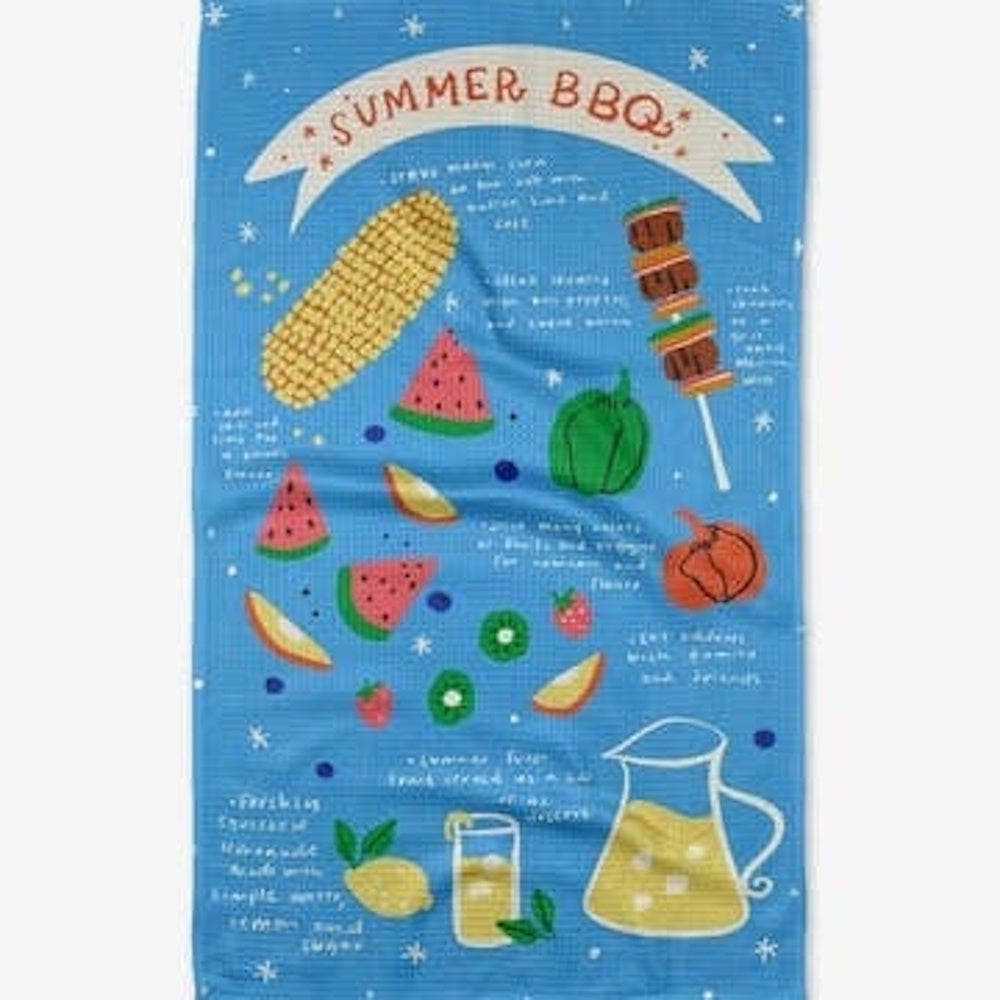 A blue tea towel featuring "SUMMER BBQ" text with illustrations of corn, watermelon, a skewer, and lemonade.