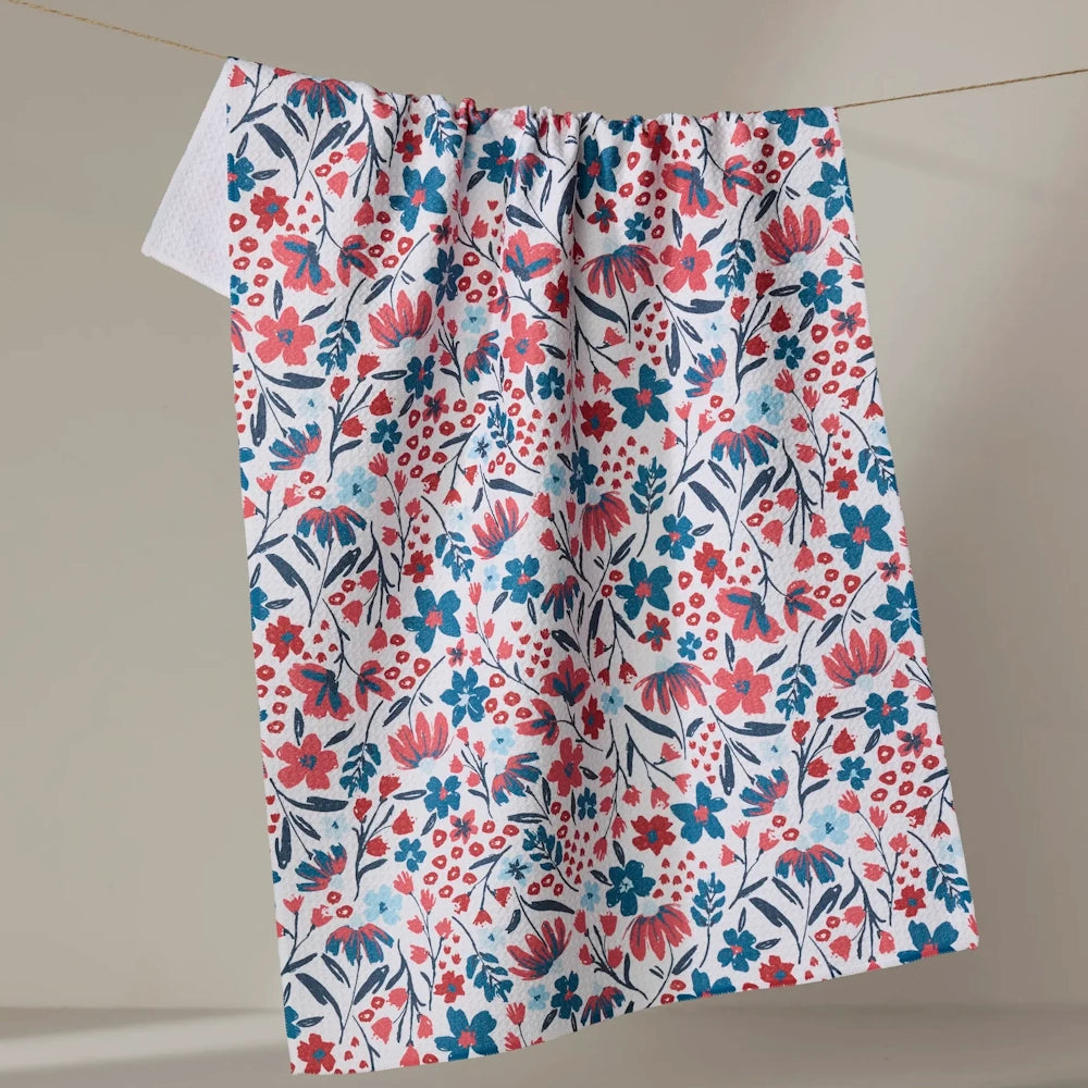 A tea towel with a red and blue floral pattern hanging on a clothesline against a neutral background.