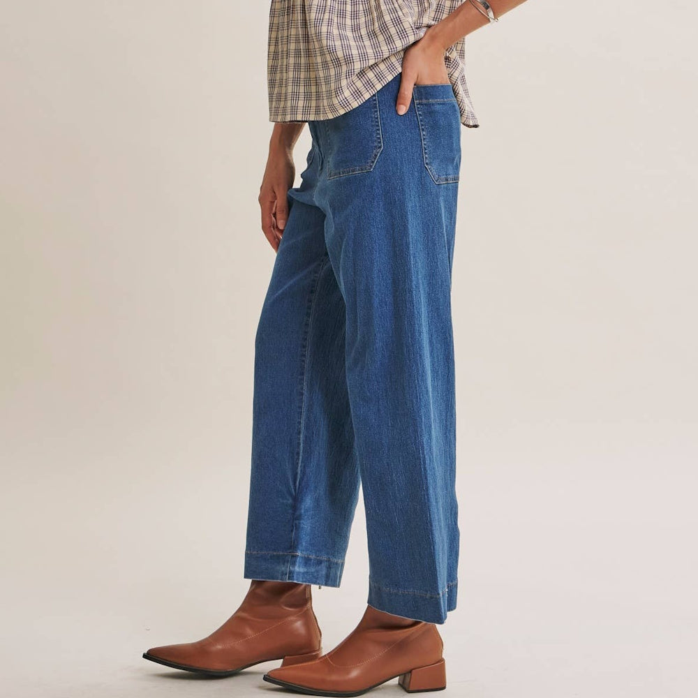 Side profile of a person wearing ankle-length wide-leg blue denim jeans paired with brown leather boots.