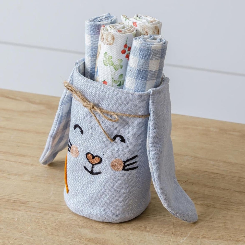 A light blue bunny-shaped fabric holder filled with rolled, patterned cloths on a wooden surface.