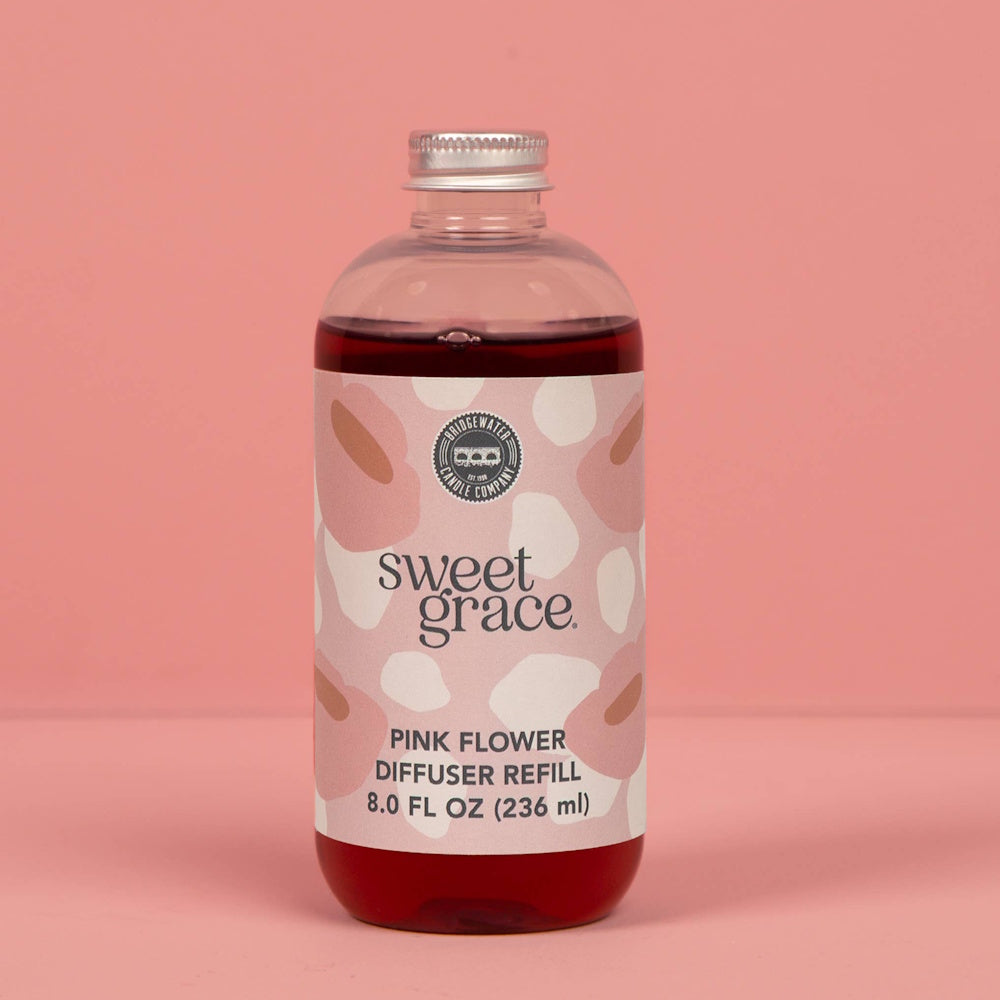 Sweet Grace Pink Flower Diffuser Refill bottle filled with dark liquid against a solid pink background.