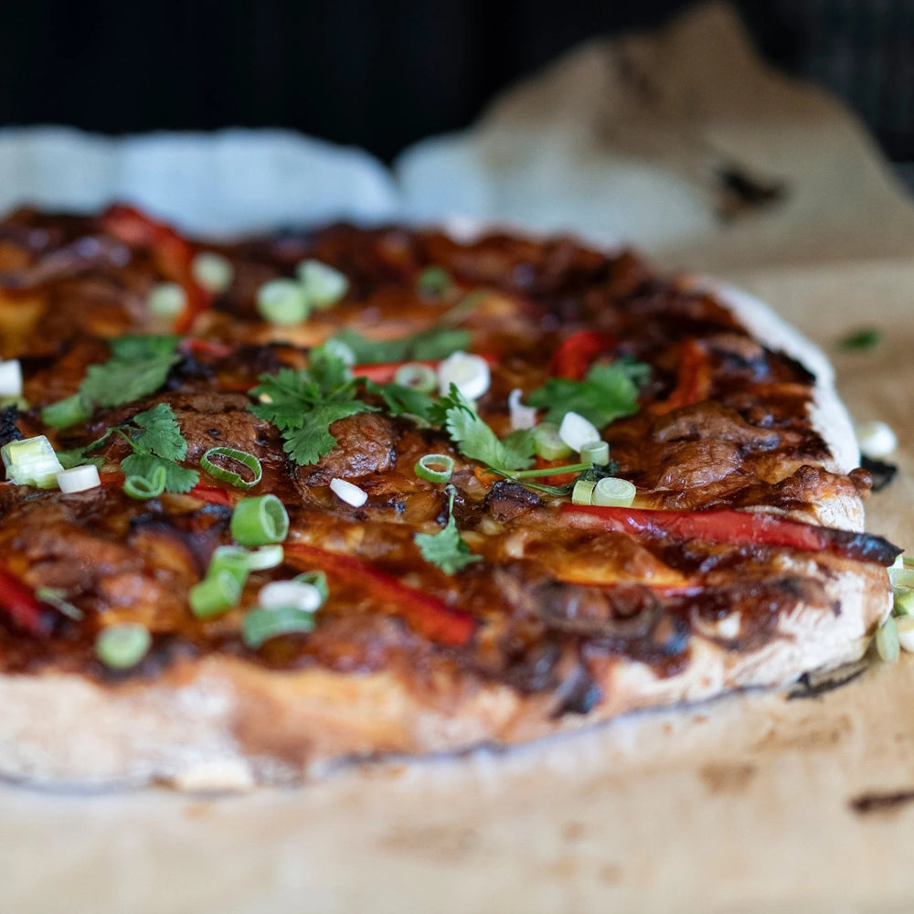 Homemade BBQ pizza topped with red peppers, fresh cilantro, and green onions on parchment paper.