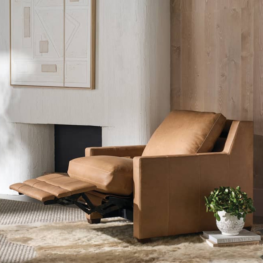 Modern tan leather recliner chair in a minimalist living room with a white fireplace and light wood wall.