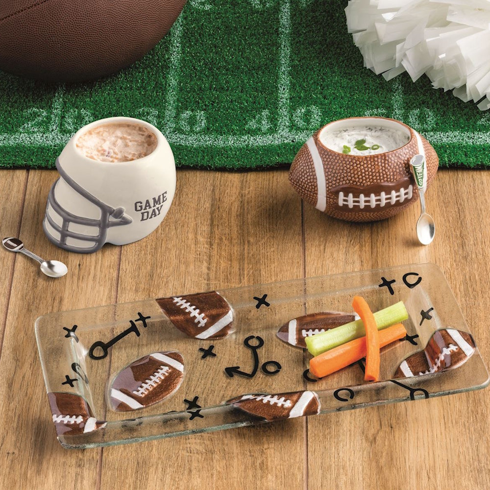 Football and helmet dip bowls with small spoons next to a glass platter with snacks and playbook design.