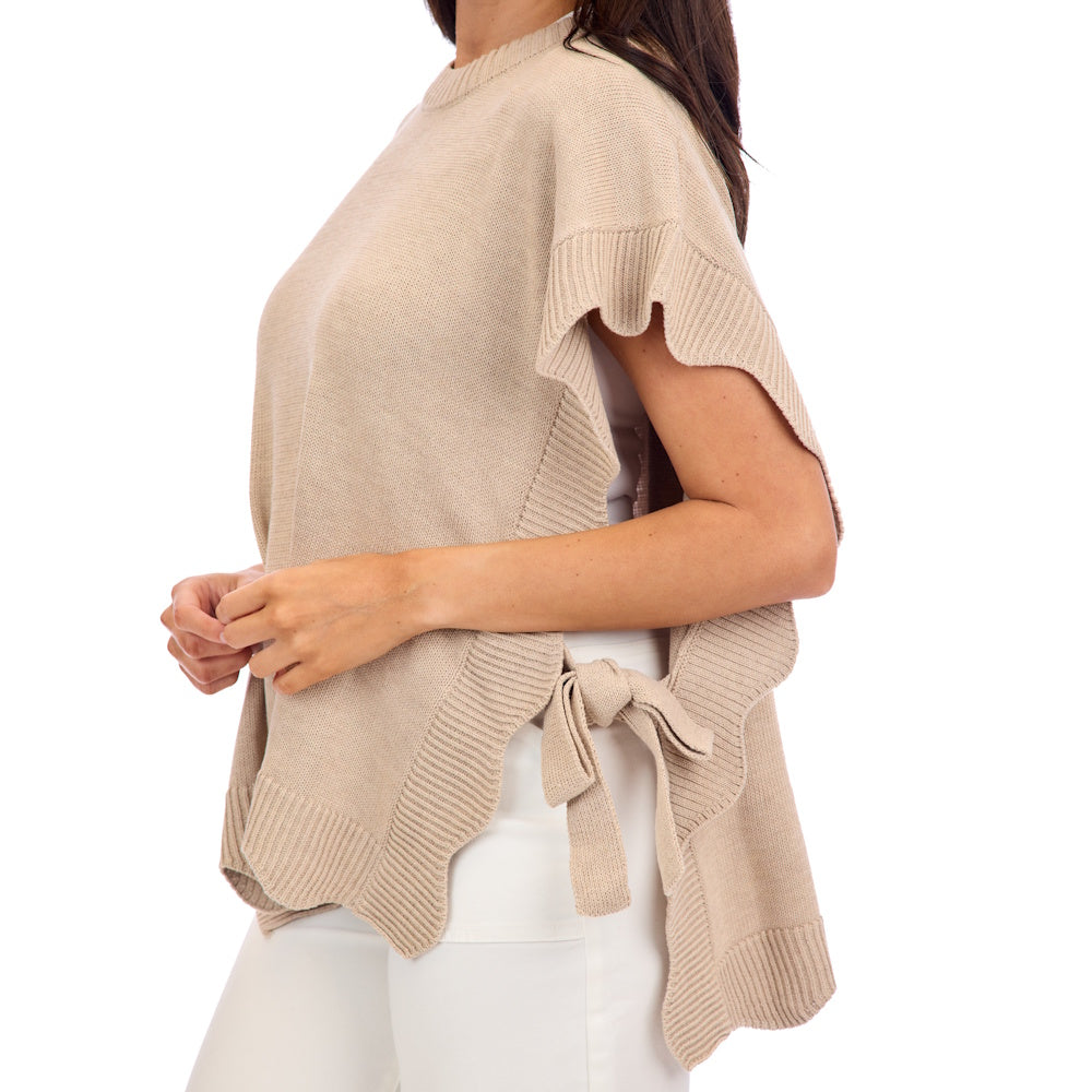 Side profile of a woman wearing a tan short sleeve knit sweater with scalloped edges and a side-tie bow.