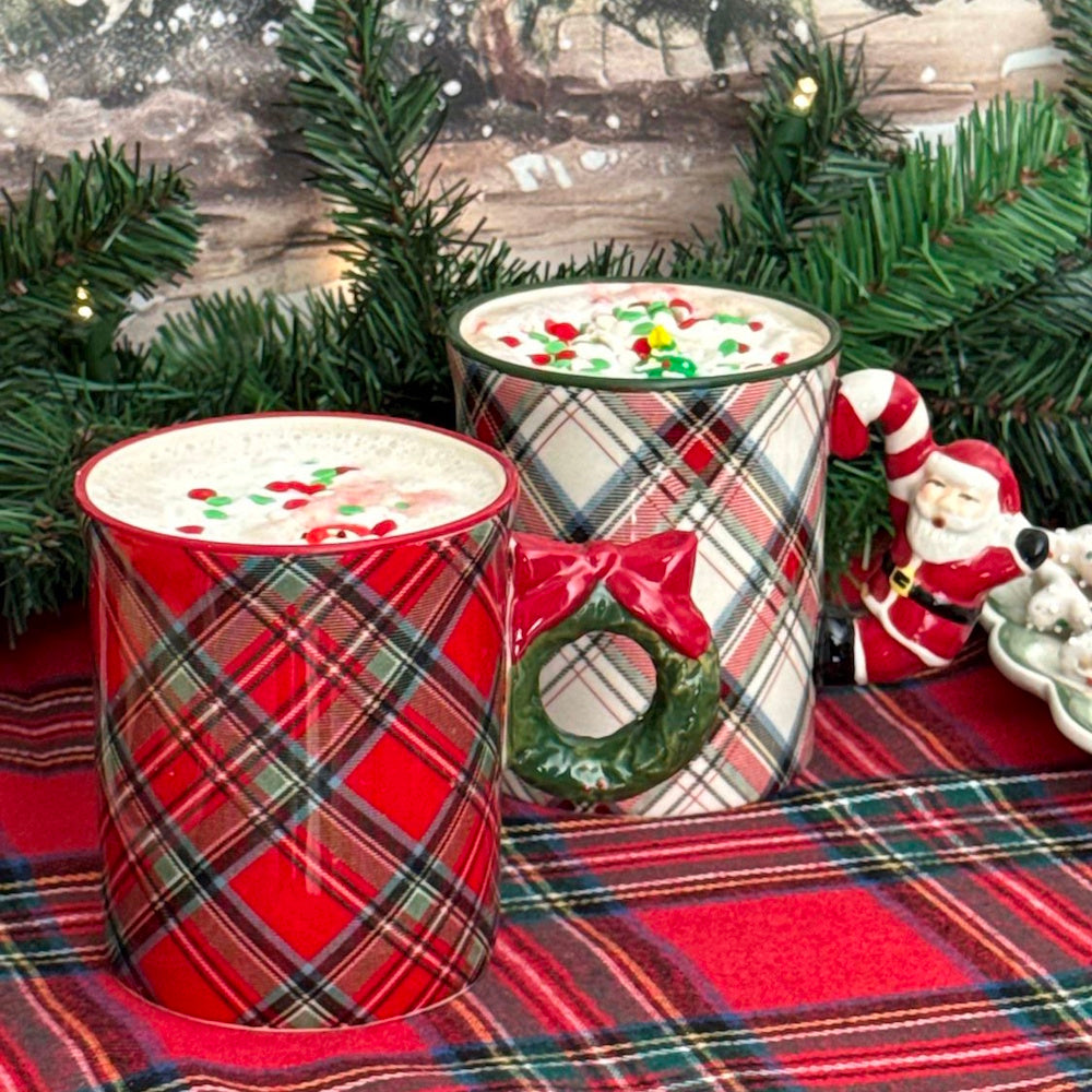 Two tartan plaid holiday mugs with figural handles filled with drink in front of pine greenery.